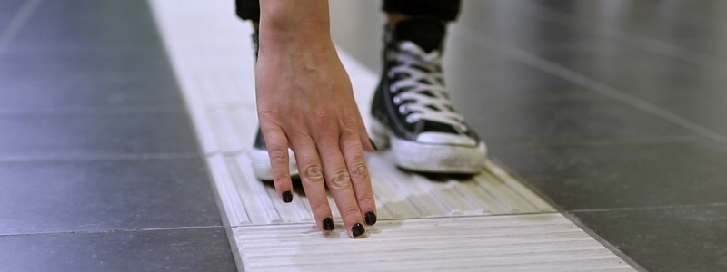 En hånd kjenner på et riflete ledefelt for blinde i et gulv.