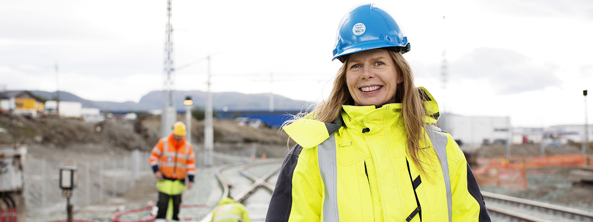Illustasjonsbilde: Jernbaneanlegg med kvinne i hjelm og arbeidstøy i forgrunnen.