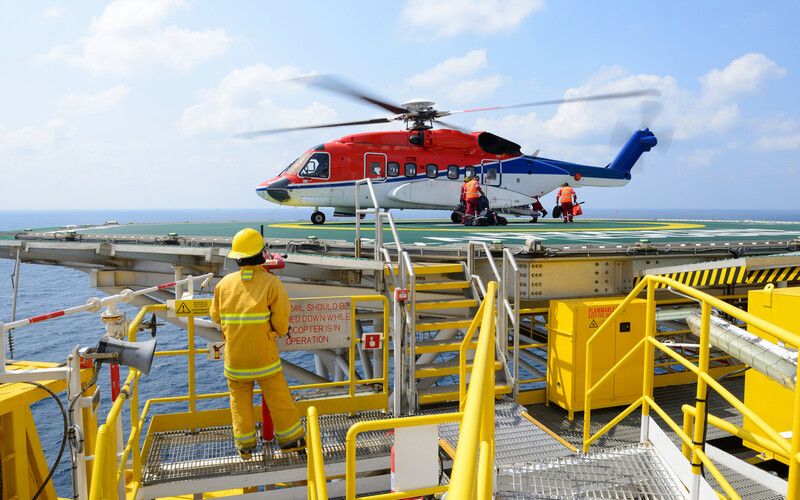 To mennesker er på vei inn i et helikopter som står på landingsplass på en oljeplattform. Foto.