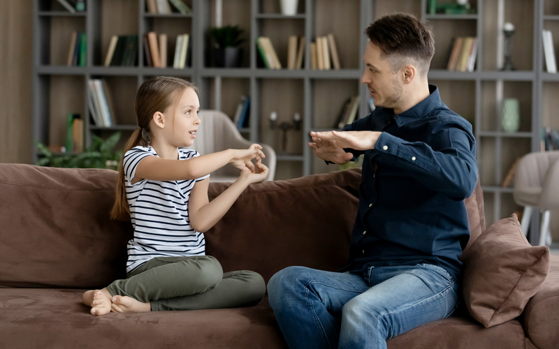 Jente og mann sitter i en sofa og kommuniserer med tegnspråk.