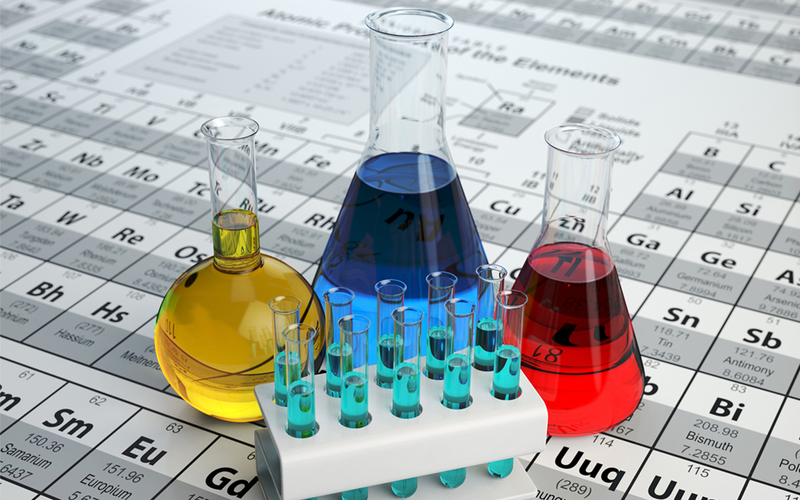 Reagensrør og kjemiflasker med ulike farger plassert på periodesystemet