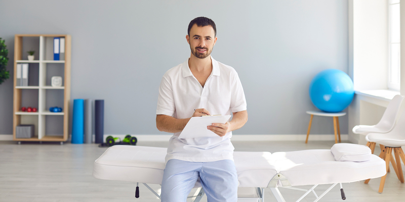 Mann kledd i arbeidstøy for helsepersonell sitter på behandlingsbenk og gjør notater.