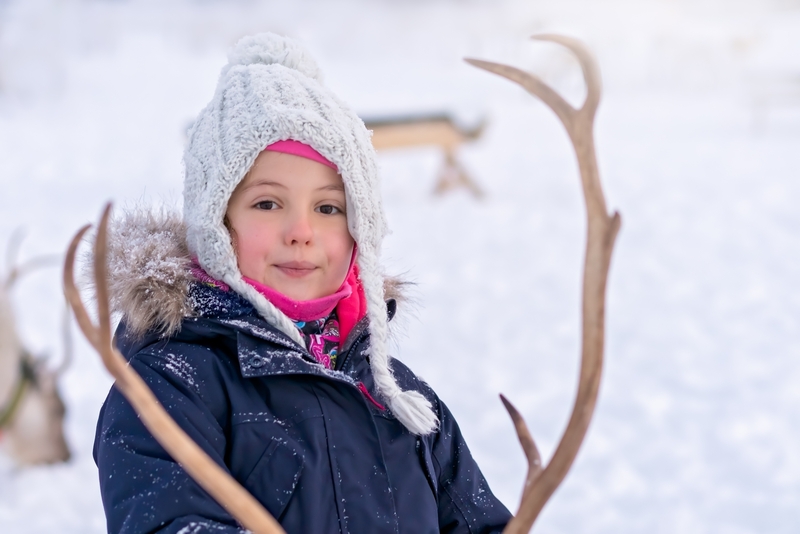 Liten jente som mater et reinsdyr og ser midt i kameraet.